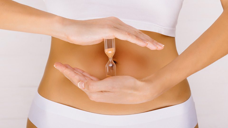 Frau hält Sanduhr vor ihrem Bauch – Kinderwunsch Kö