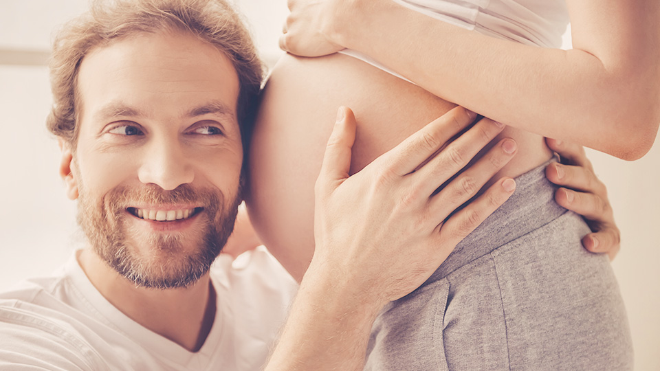 Mann horcht an Bauch einer schwangeren Frau – Kinderwunsch Kö